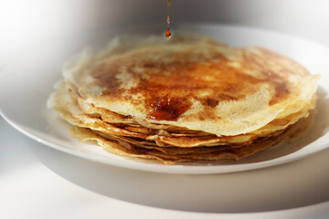 Slavic thin fried pancakes with a crispy ruddy crust in a stack with a dripping drop of maple syrup