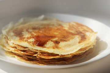 Slavic thin fried pancakes with a crispy ruddy crust in a stack with maple syrup and a flying drop