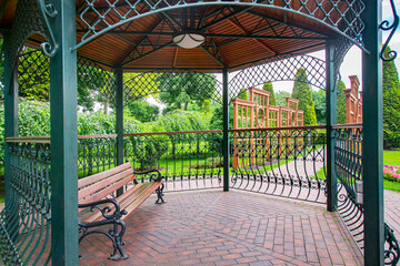 iron gazebo with ceiling lighting for relaxing on a wooden bench in the backyard with vertical pergola for growing plants in a park with bushes and trees on a green lawn parkland, nobody.