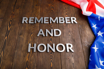 words remember and honor laid with silver metal letters on wooden background with USA flag on the...