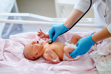 Unrecognizable female doctor examines infant baby girl with stethoscope in maternity ward at...