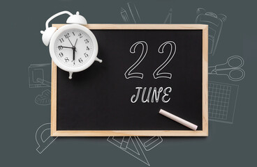 june 22. 22th day of month, calendar date.   Blackboard with piece of chalk and white alarm clock on green background. Concept of day of year, time planner, summer month