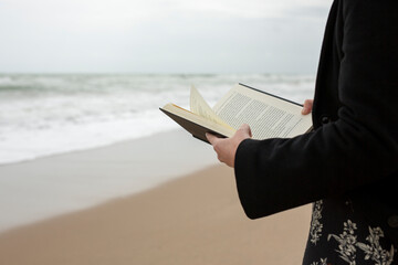 Plano de un libro no identificable con tapas negras sostenido en las manos de una mujer en la playa...
