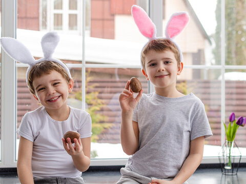 Two boys with rabbit ears on their heads playing with chocolate eggs