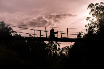 silhouette of a girl sitting on a suspended bridge watching the sunset