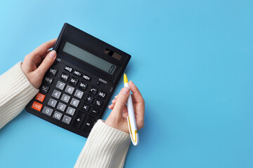 A black calculator in his hands on a blue background. Symbol of data counting and problem solving