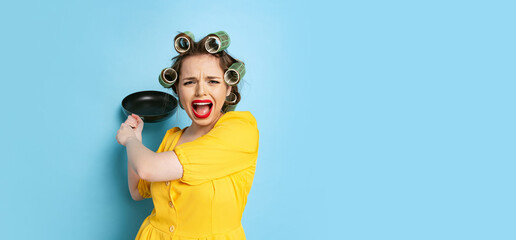 Comic portrait of young emotional girl, housewife with curlers on her head holding pan isolated on...
