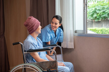 A smiling young Asian female nurse having fun talking with an Asian male cancer patient in a head...