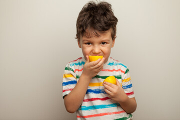 little boy eating lemon, sour taste, makes grimace, facial emotions negative, in white striped T-shirt, isolated white background, copy space.
