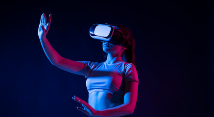 Modern architect using virtual reality glasses at workplace and touch something in virtual world. Woman working in VR goggles in neon light. Designer working in VR studio.