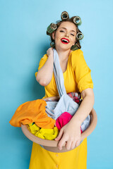Comic portrait of young emotional girl, housewife with curlers on her head isolated on blue studio...