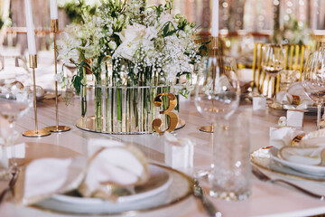 Wedding banquet. On the festive table are plates with decorative napkins, glasses, candles and cutlery. The table is decorated with flowers