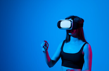 Portrait of young woman playing in VR-glasses in neon light on blue background. Concept modern gadgets and technologies. Future technology concept. Virtual reality gaming.