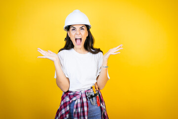 Young caucasian woman wearing hardhat and builder clothes over isolated yellow background clueless...