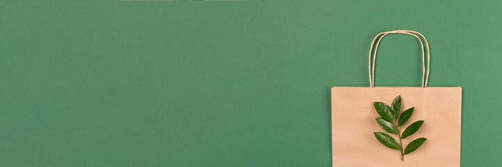 Recycled kraft paper bag with green leaves on green background. Sustainable shopping packaging concept. Green shopping. Banner with copy space