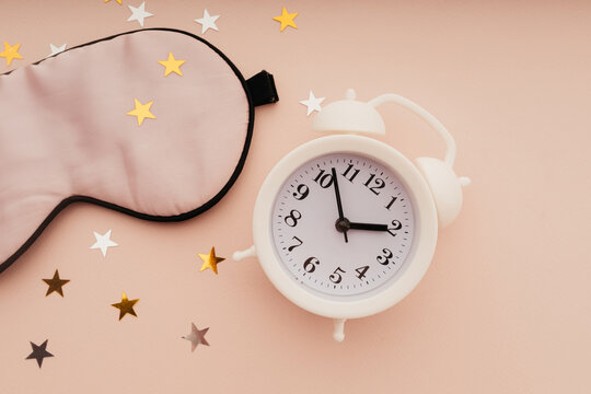 Concept eye protection from light for good sleep. Sleeping mask, alarm clock and paper stars on pink background close-up