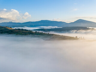 Flight over fog in Ukrainian Carpathians in summer. Mountains on the horizon. A thick layer of fog covers the mountains with a continuous carpet. Aerial drone view.