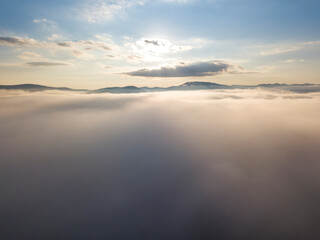 Fototapeta na wymiar Flight over fog in Ukrainian Carpathians in summer. Mountains on the horizon. A thick layer of fog covers the mountains with a continuous carpet. Aerial drone view.