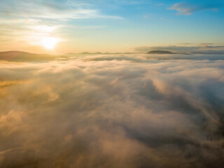 The rays of dawn over the fog in the Ukrainian Carpathians. Aerial drone view.