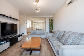 Apartment living room with double wooden coffee table, fabric upholstered sofa and large flat tv on white and gray sideboard