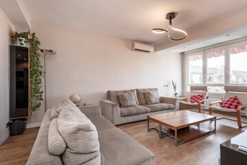Apartment living room with double wooden coffee table, fabric upholstered sofa, large window, aluminum radiators and air conditioning