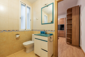 Bathroom with blue glass vanity, matching framed mirror and varnished pine door with valance on the walls and exit to a bedroom with wooden furniture and oak flooring