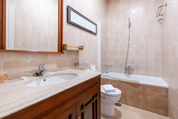 A corner shot of a bathroom with a white porcelain sink set on a marble countertop over dark wood to match the mirror