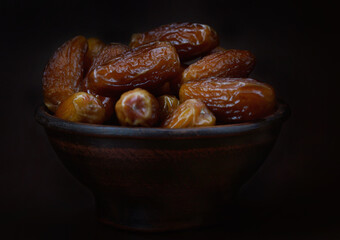 Clay bowl of ripe beautiful dates. Dried dates on a brown background.