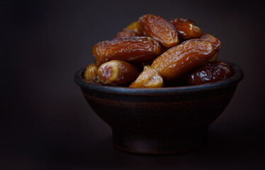 Clay bowl of ripe beautiful dates. Dried dates on a brown background.