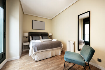 Bedroom with towels on the bed, gray fabric upholstered headboard, black framed mirror and green velvet upholstered chair in vacation rental apartment