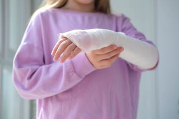 Close-up of a broken arm of a child in a cast. The girl holds her hand folded against. A child with...