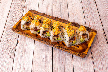 Sushi uramaki dragon roll with soy sauce, avocado, nori seaweed, red tuna, chives on a wooden plate