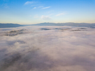 Flight over fog in Ukrainian Carpathians in summer. A thick layer of fog covers the mountains with a solid carpet. Mountains on the horizon. Aerial drone view.