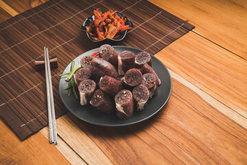 Blood sausage or Sundae in black plate on wooden table background.