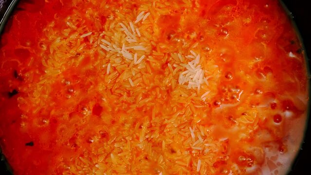Jollof rice cooking. Rice with tomato paste, tomatoes, spices is cooked in a pan. Top view.