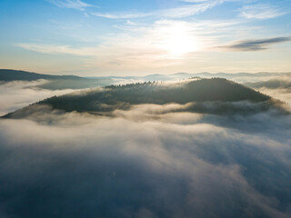 Sunny morning in the foggy Carpathians. A thin layer of fog covers the mountains. Aerial drone view.
