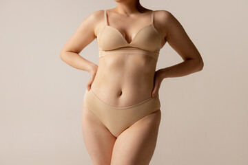 Cropped portrait of natural looking female body in beige underwear posing isolated over light studio background - obrazy, fototapety, plakaty