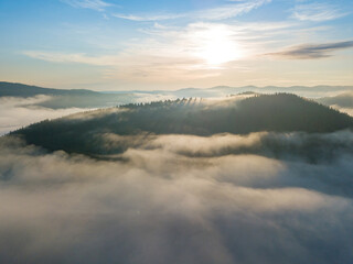 Sunny morning in the foggy Carpathians. A thin layer of fog covers the mountains. Aerial drone view.