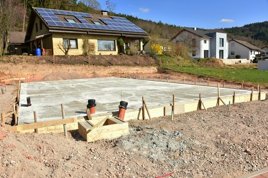 Frisch betonierte Bodenplatte mit Anschlüssen für ein frei stehendes Haus in einem Neubaugebiet