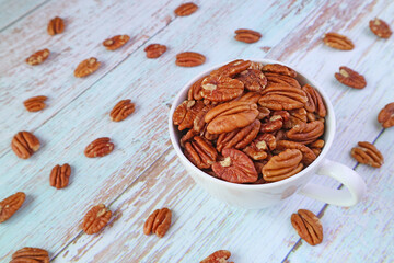 A Cup Full of Pecan Nuts with Some Kernels Scattered around on Wooden Table