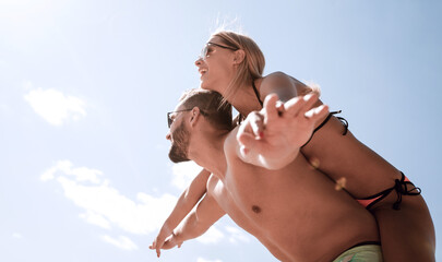 Man carrying woman piggyback on beach.