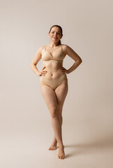 Full-length portrait of young beautiful woman posing in beige underwear isolated over studio...