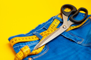 measuring tape is threaded into jeans on a yellow background, next to scissors, close-up. The...