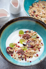 Greek yogurt with granola and grapes served in a turquoise bowl, vertical shot, close-up