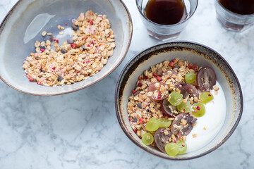 Bowls with granola, grapes and yogurt for breakfast, high angle view on a light-grey marble background, studio shot