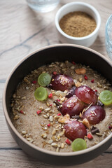 Bowl of flaxseed porridge served with sliced red and green grapes, vertical shot on a brown wooden background, closeup