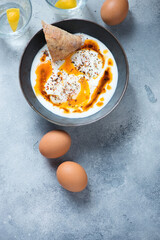 Bowl with turkish traditional cilbir on a light-blue stone background, vertical shot with space, top view