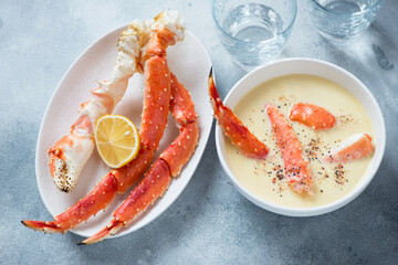 Corn cream-soup served with boiled kamchatka crab legs, horizontal shot on a light-blue stone background, selective focus