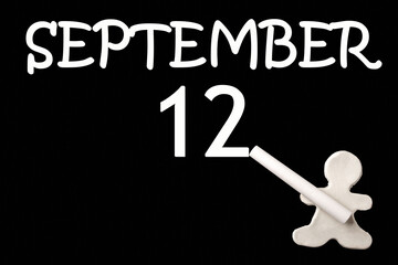 A small white plasticine man writing the date 12 September on a black board. Business concept. Education concept.