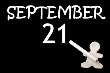 A small white plasticine man writing the date 21 September on a black board. Business concept. Education concept.